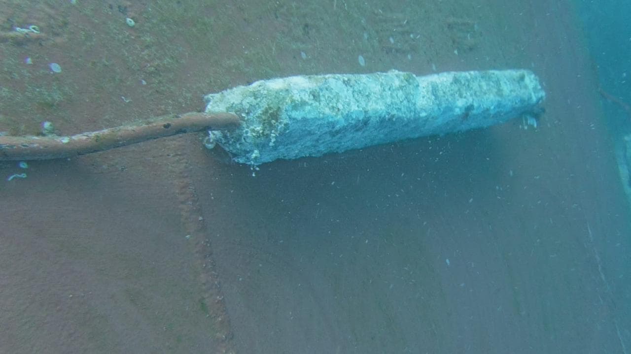 Underwater view of the same hull panel with the cylindrical fixture and cable visible