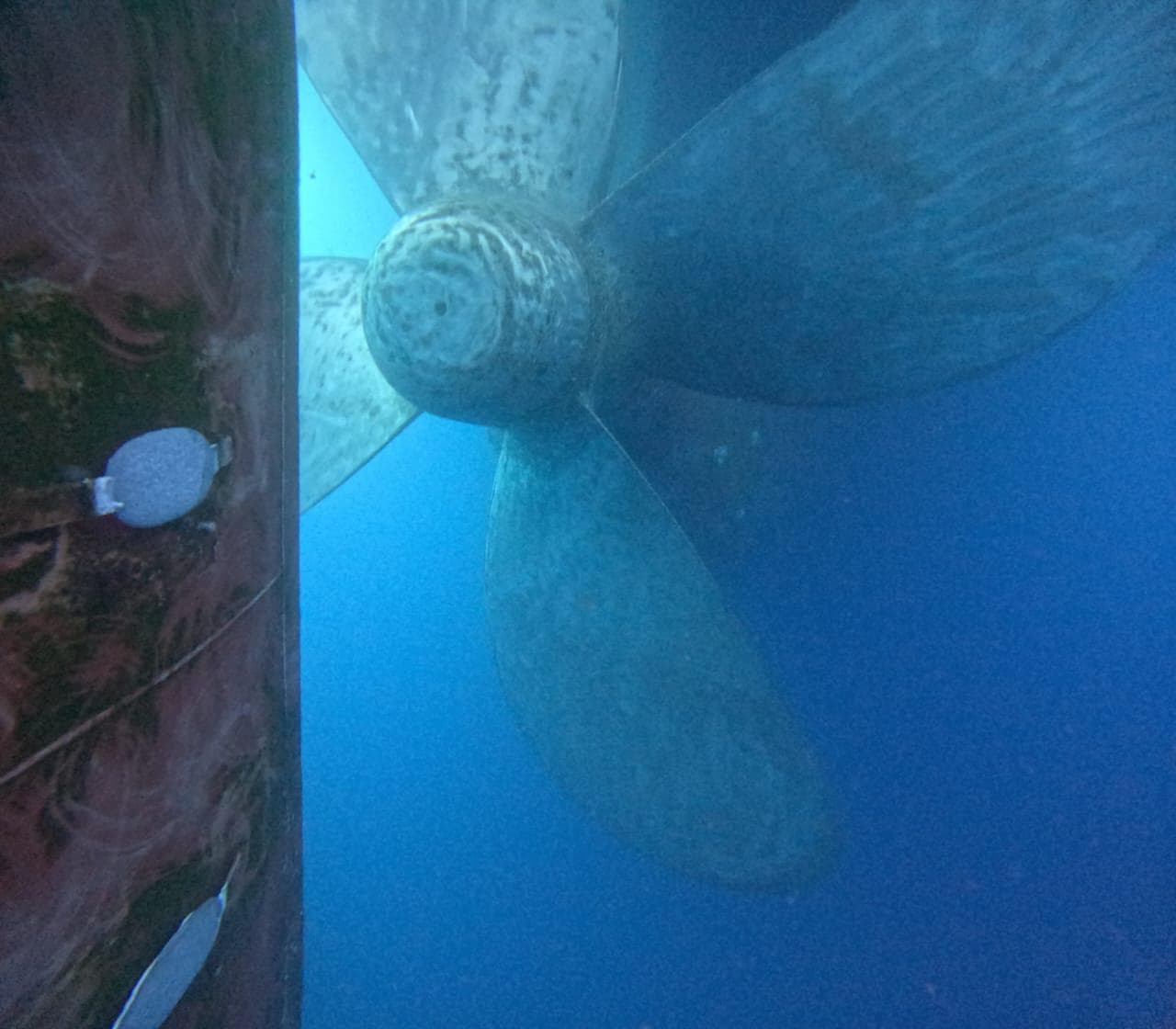 Oblique underwater view of a propeller and adjacent hull edge in blue water
