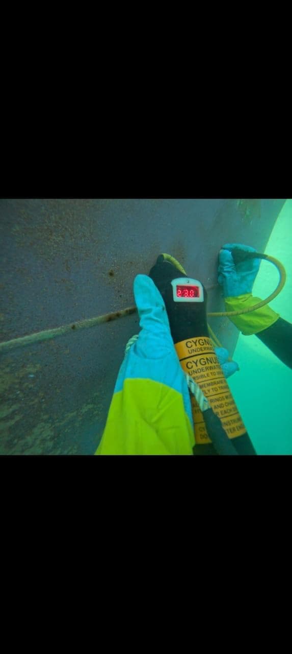 Commercial diver using an underwater thickness gauge against ship hull plating